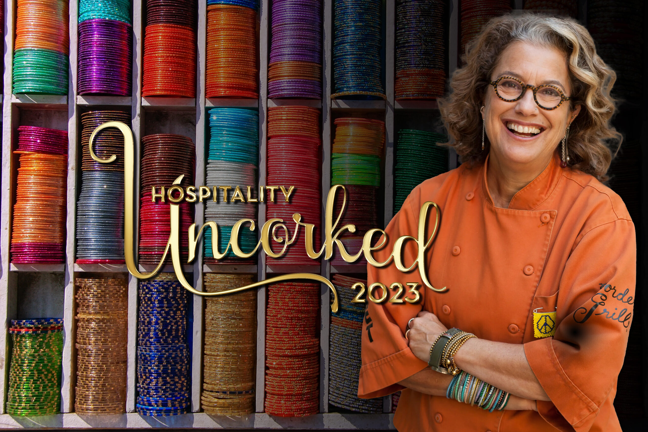 Susan Feniger wearing a orange chef coat in front of a colorful background